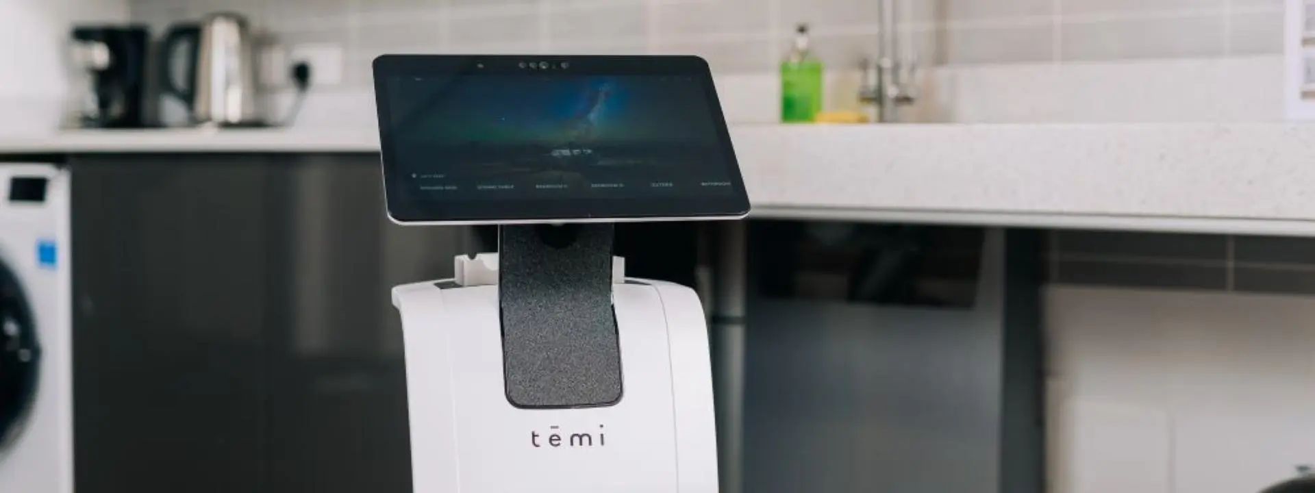A white Temi service robot with a large touchscreen stands in the foreground of a modern kitchen