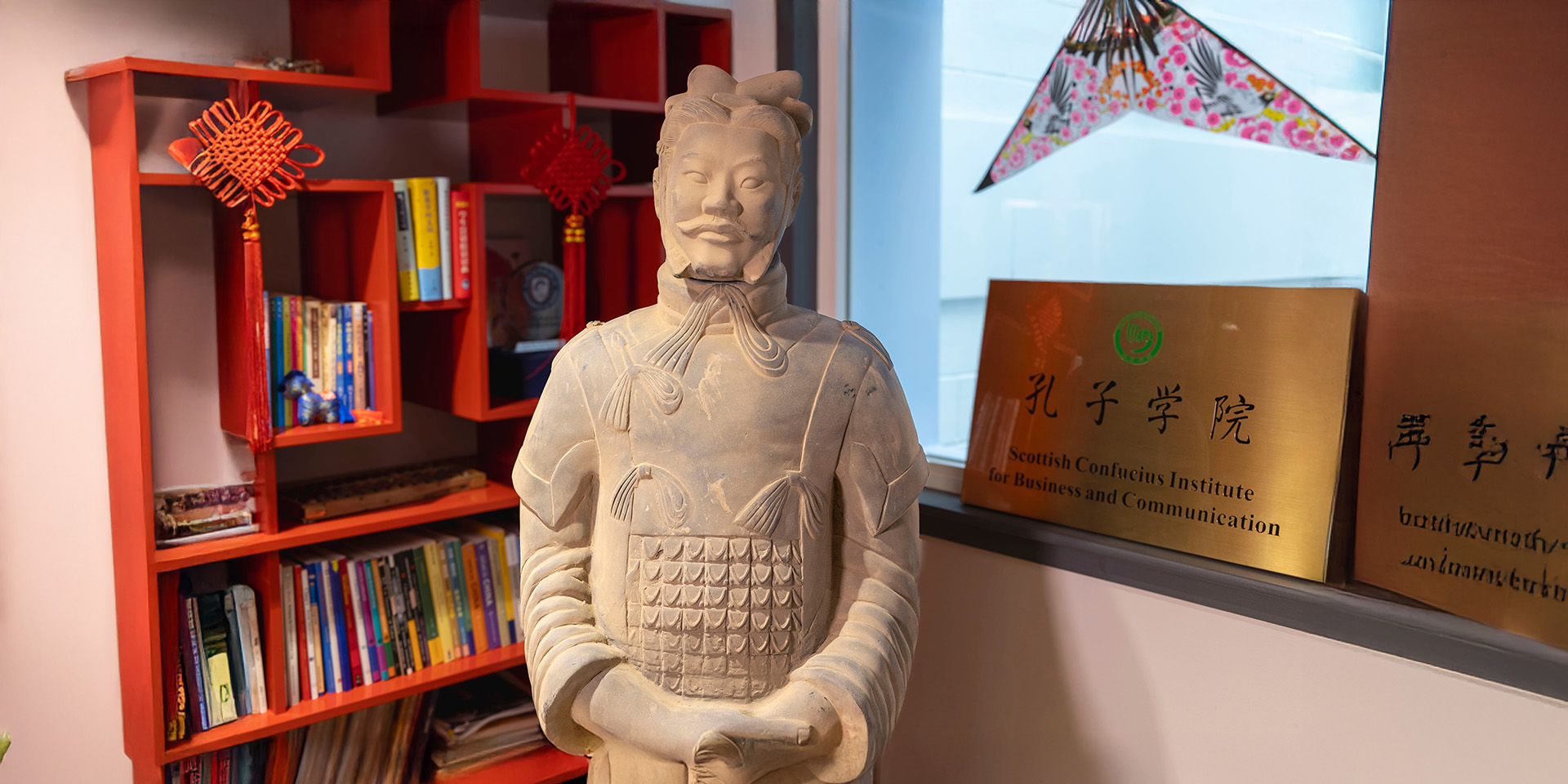 Terracotta warrior statue head and shoulders in Confucius Institute with bookshelf behind 