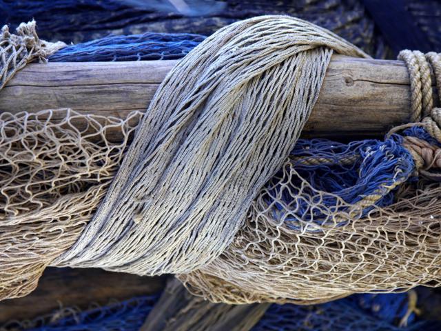 A weathered wooden beam wrapped with various trawling ropes and nets.
