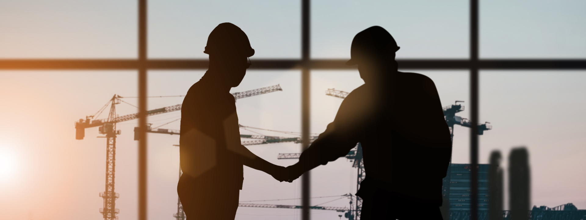 Two silhouetted construction workers look out over a construction site.