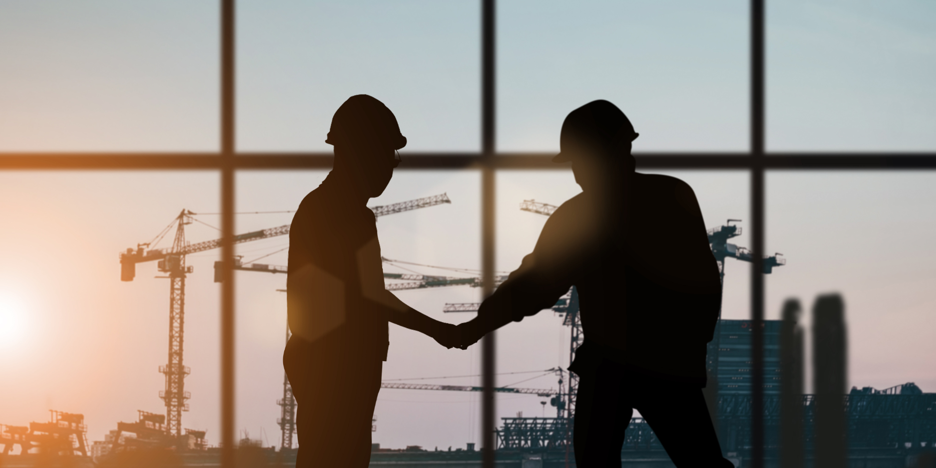 Two silhouetted construction workers look out over a construction site.