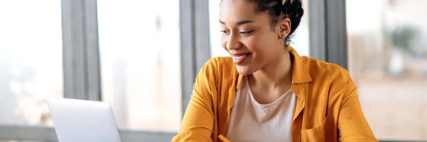 Woman works from home at a computer writing notes