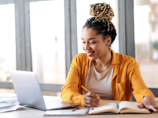Woman works from home at a computer writing notes