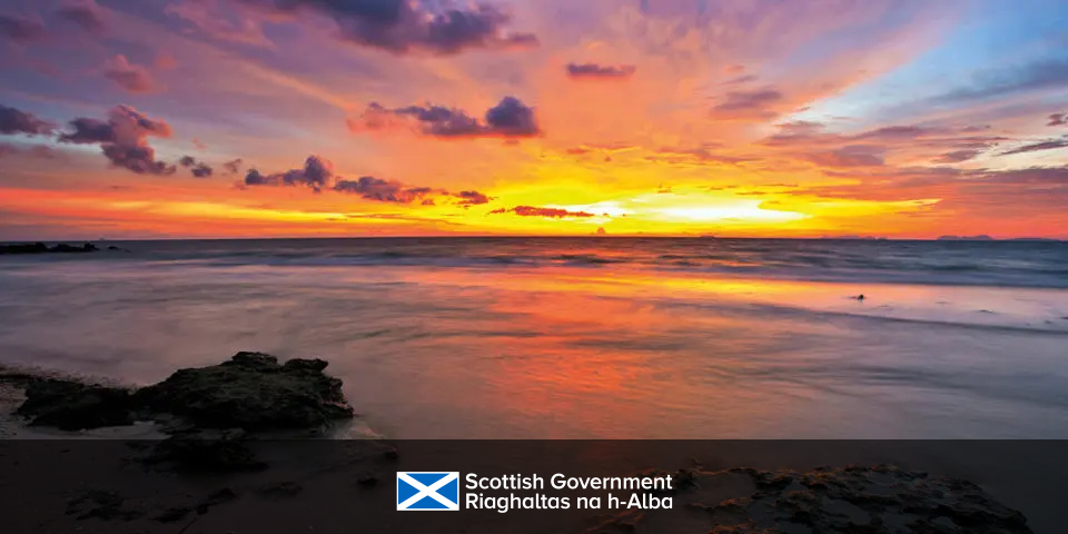 A vibrant sunset paints the sky in hues of orange, pink, and purple above a calm North Sea.