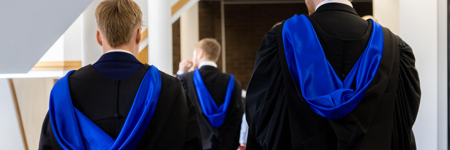 Graduates in graduate robes walking through campus