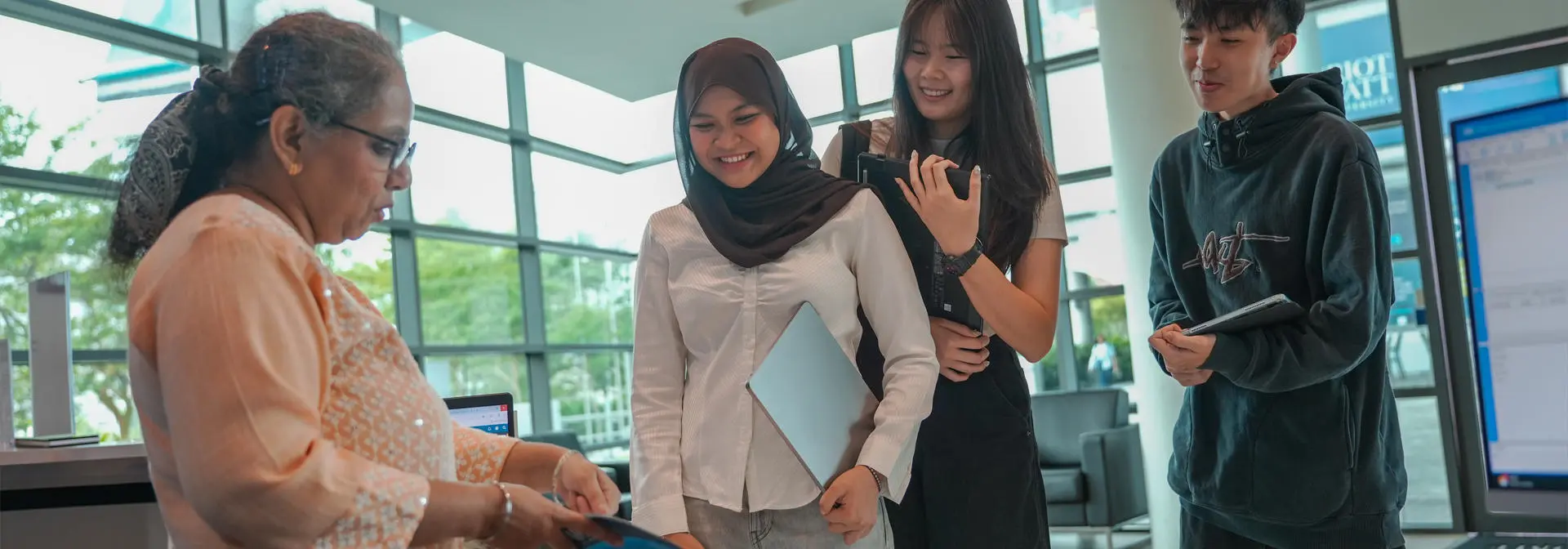 Students interact with a woman at a reception desk, discussing materials.