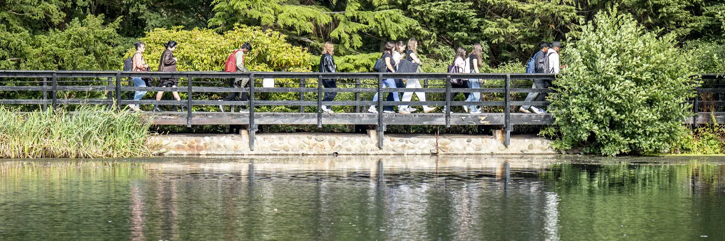 group of students cross the bridge over the Loch, with a clear sky and lush green surroundings.