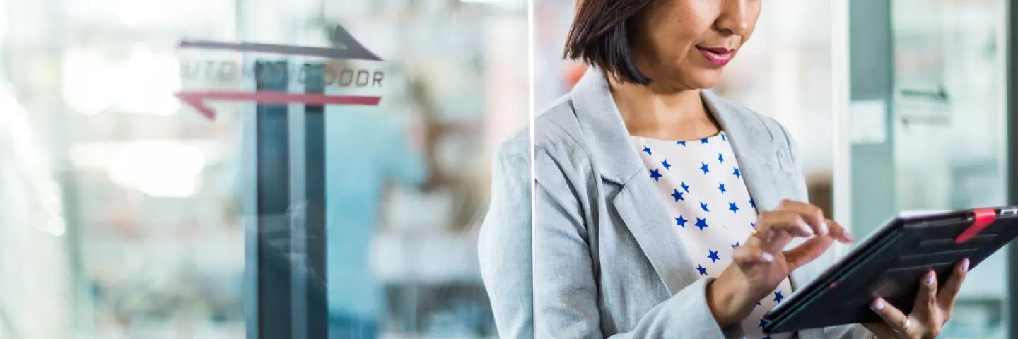 A woman stands studying information on a tablet device