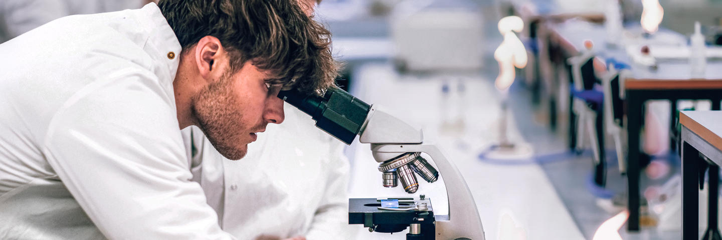 Biology student looking through microscope while his lab partner watches