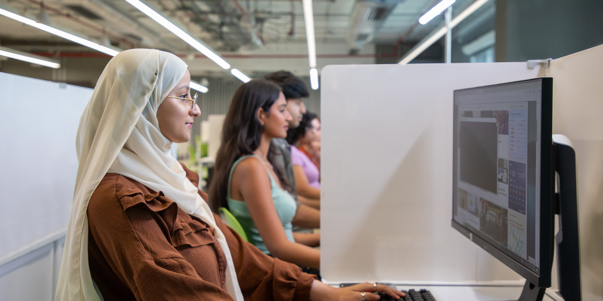 girl in hijab using computer along with other students
