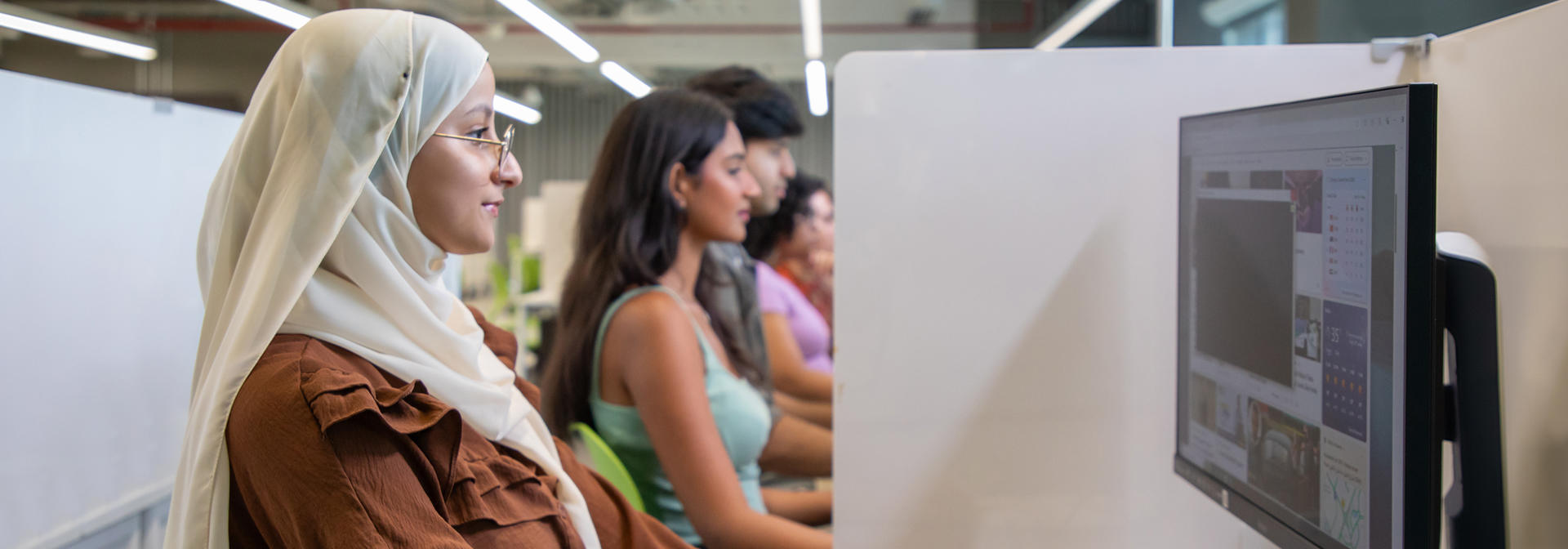 girl in hijab using computer along with other students