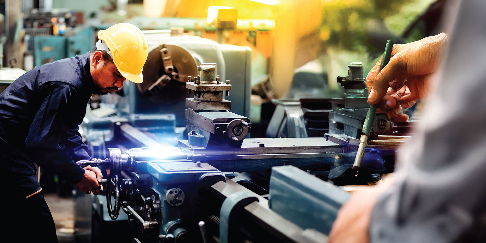 A man operates a machine in a factory, focused on his task amidst industrial equipment and surroundings.