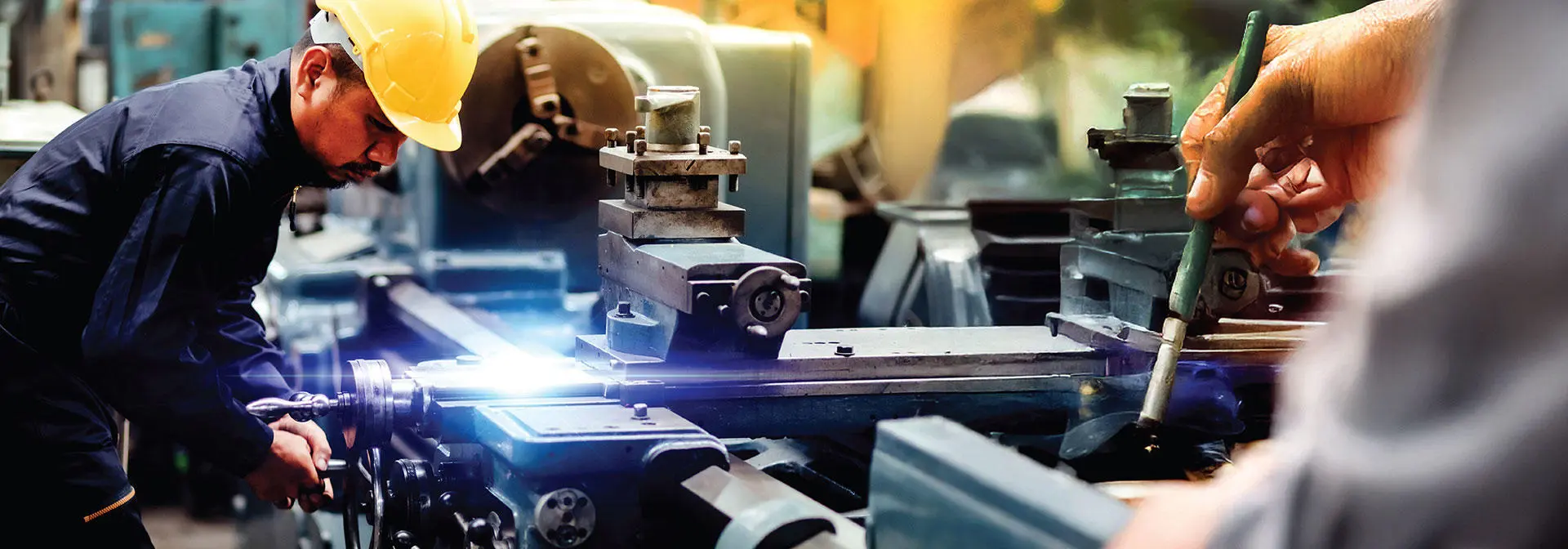 A man operates a machine in a factory, focused on his task amidst industrial equipment and surroundings.