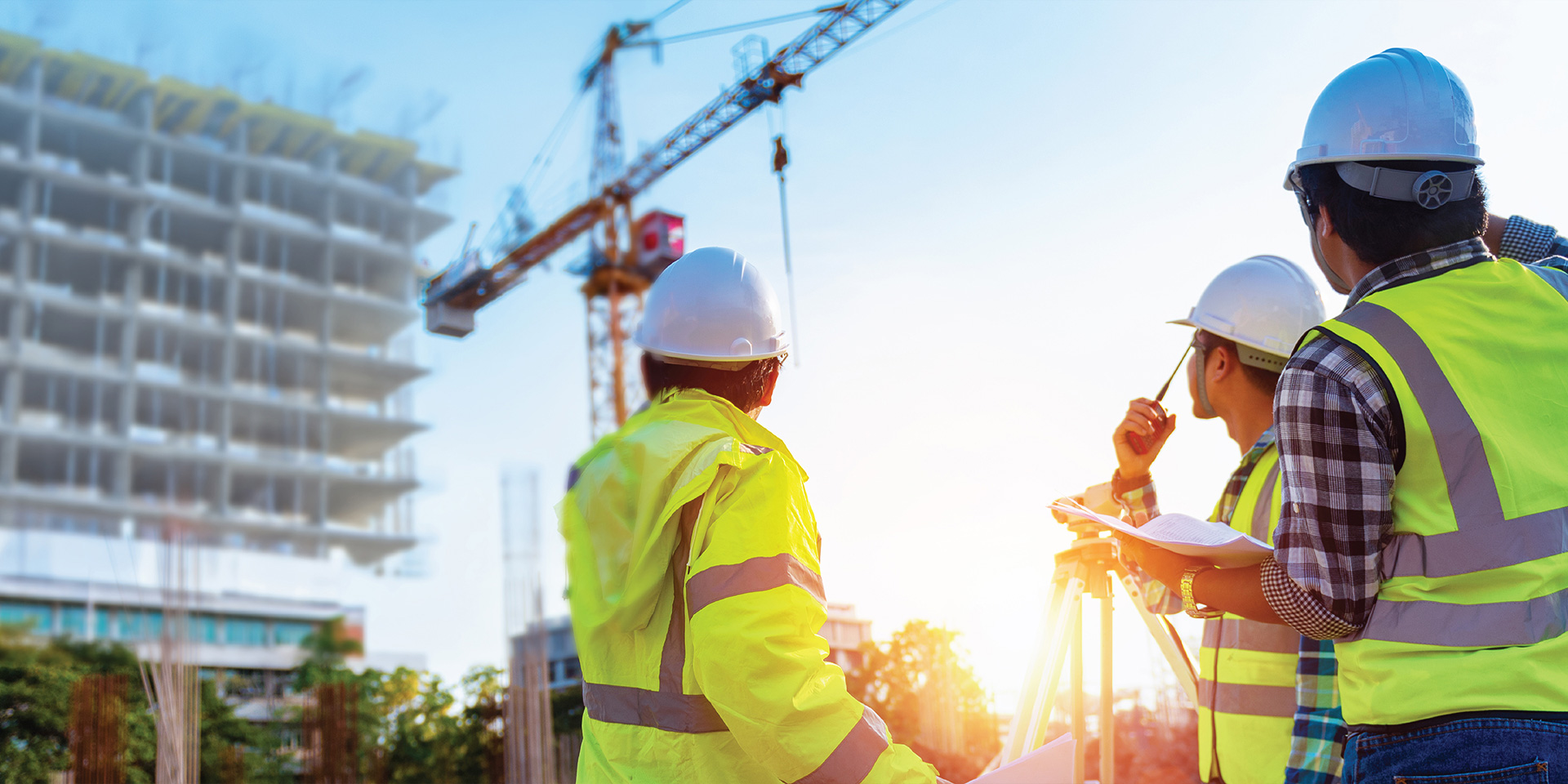 Three construction workers standing together on a construction site, wearing hard hats and safety vests.