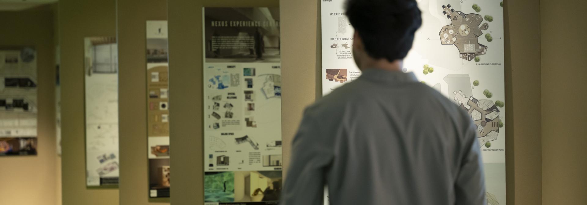 student walking past posters of architecture projects on the wall