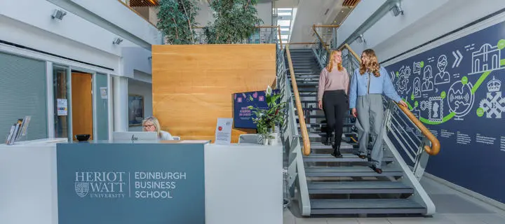Two students in the Edinburgh Business School walking down the stairs beside reception.