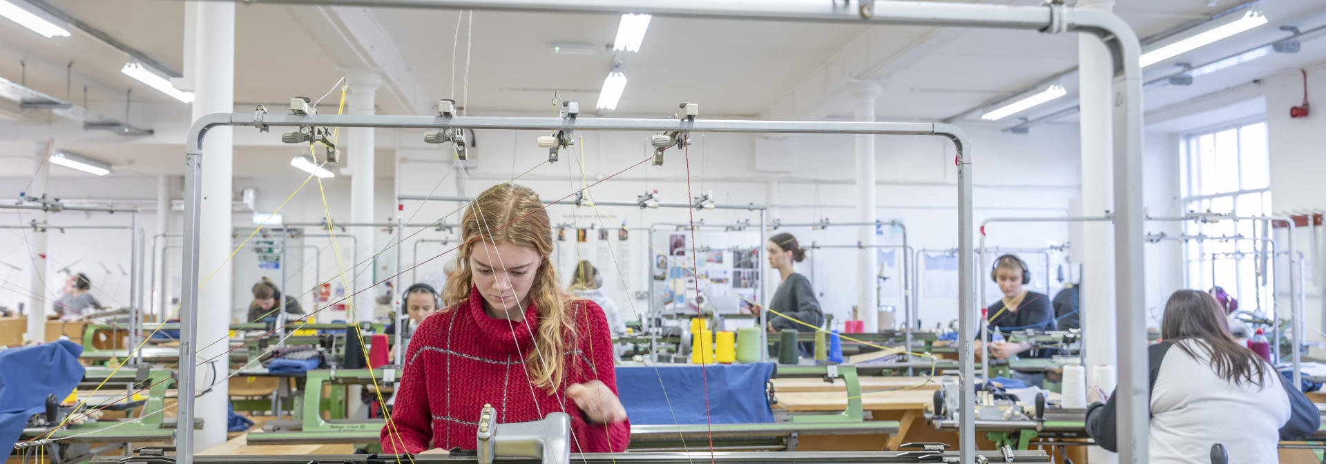 Student working on a knit machine in busy studio.