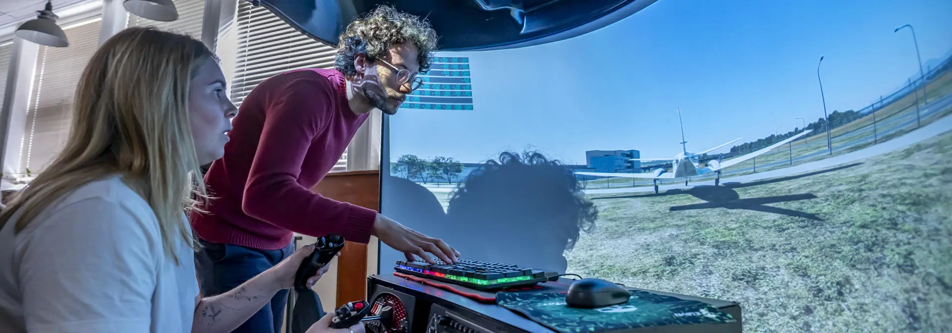 Female student on the flight simulator, being supervised by academic