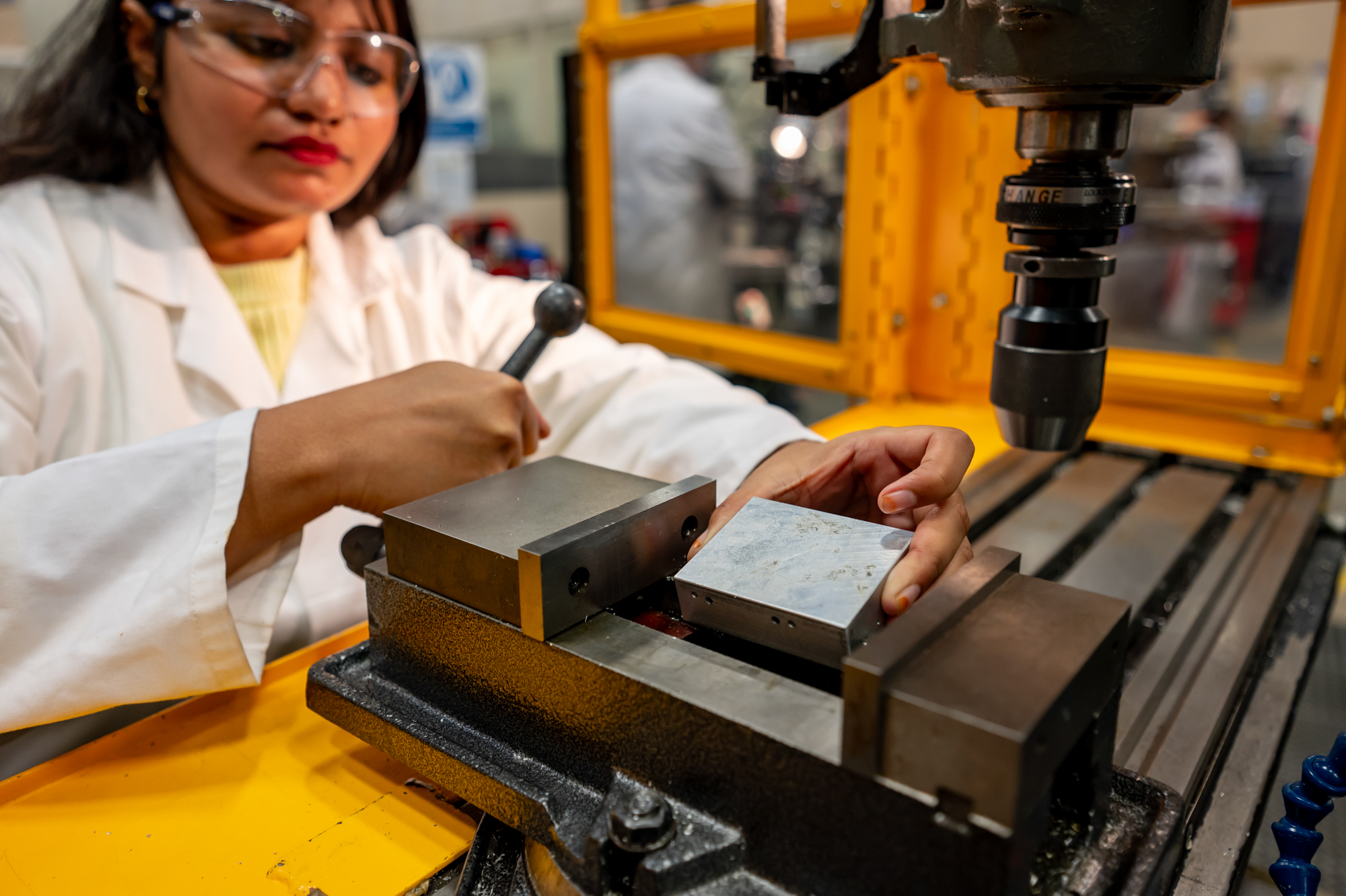 Student operating on a machine with safety goggles and a lab coat