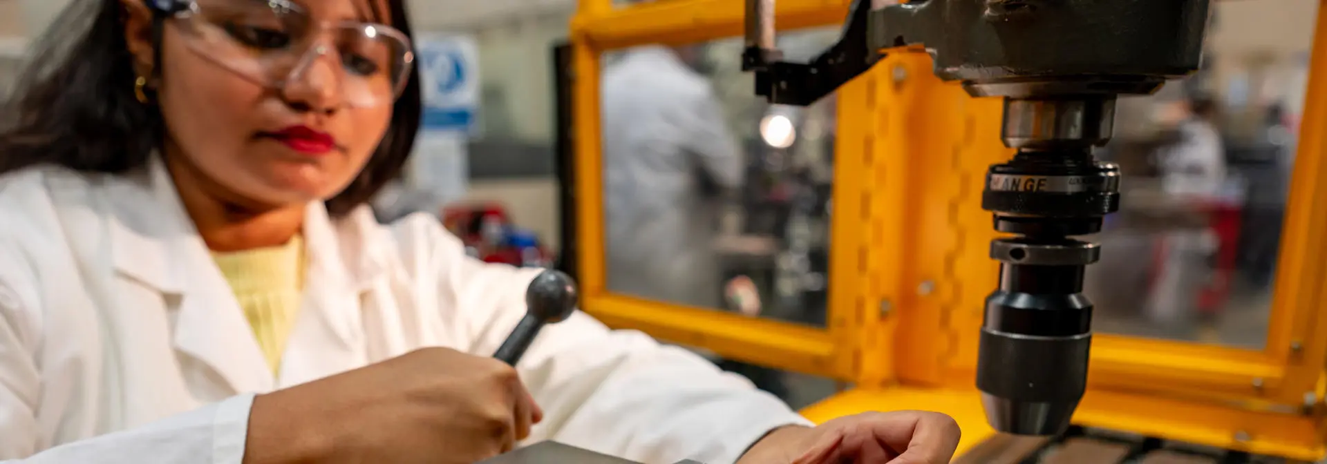 Student operating on a machine with safety goggles and a lab coat