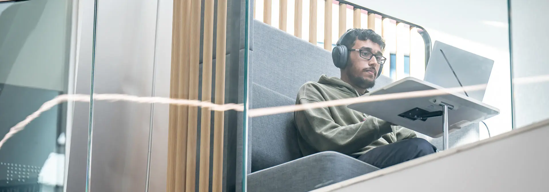 Student sitting with headphones and laptop in common area