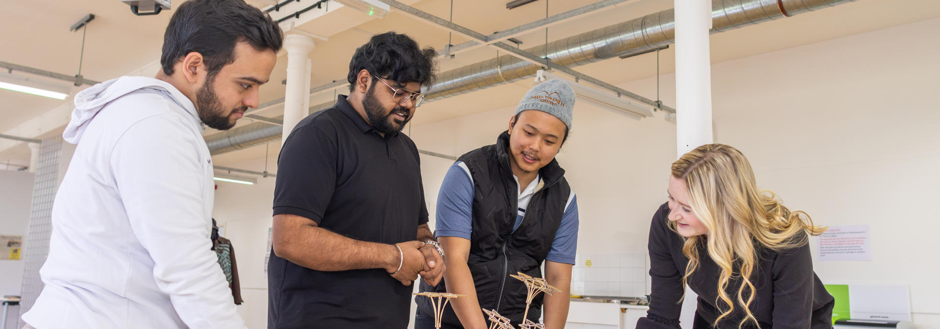 Postgraduate students discuss an intricate model design with an academic in the workspace.
