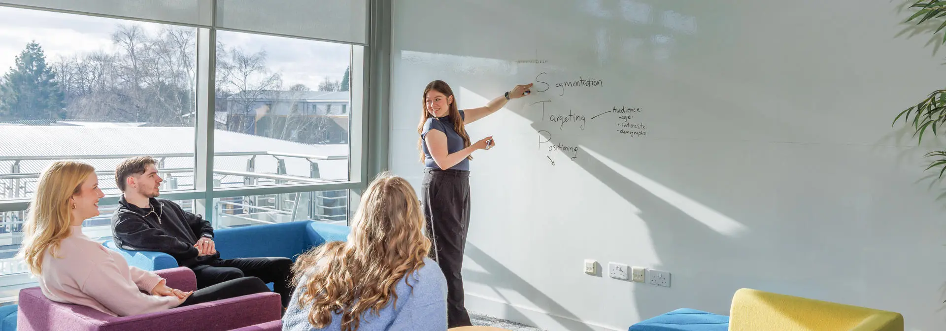 One student presenting at a whiteboard, to three students listening