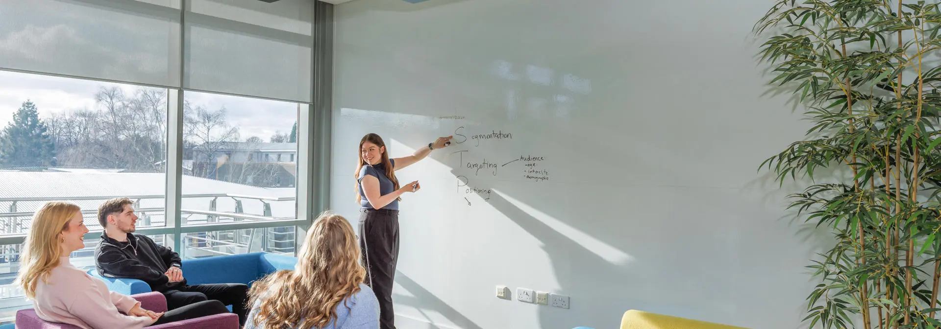 One student presenting at a whiteboard, to three students listening