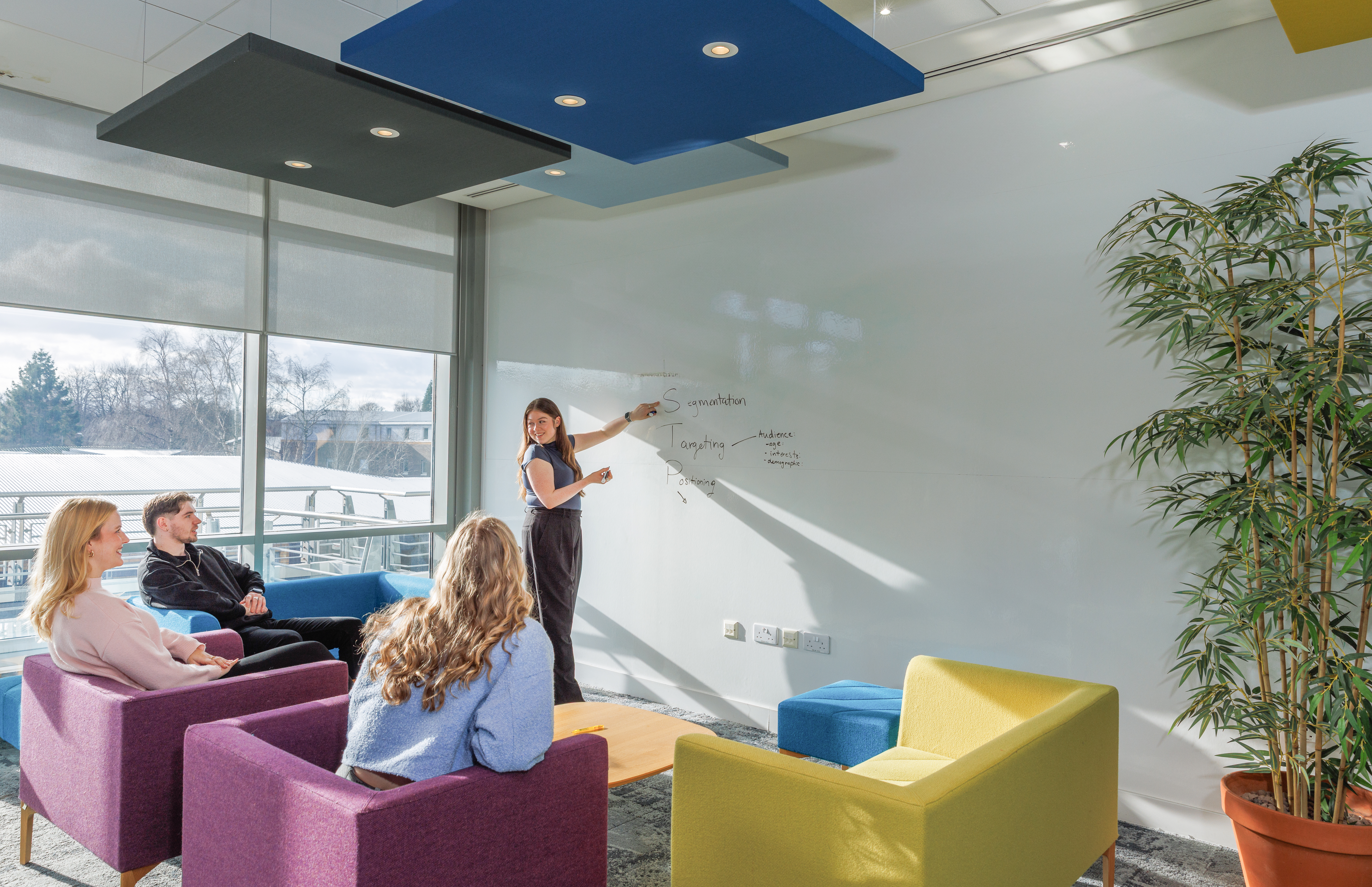 One student presenting at a whiteboard, to three students listening