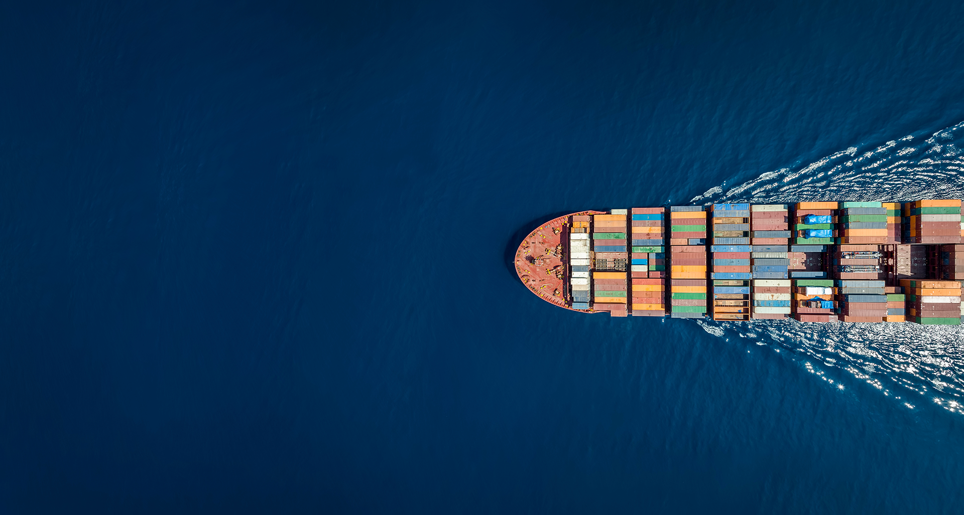 A bird's eye view of a ship containing freight containers sailing across the ocean.  