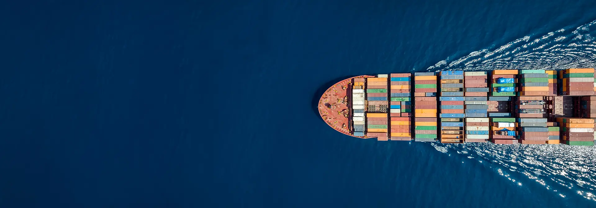 A bird's eye view of a ship containing freight containers sailing across the ocean.