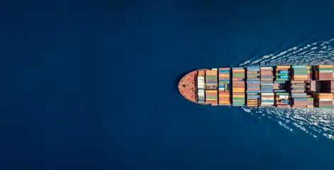 A bird's eye view of a ship containing freight containers sailing across the ocean.