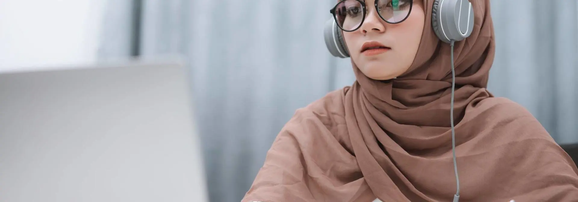 An individual working on a laptop while listening to headphones.