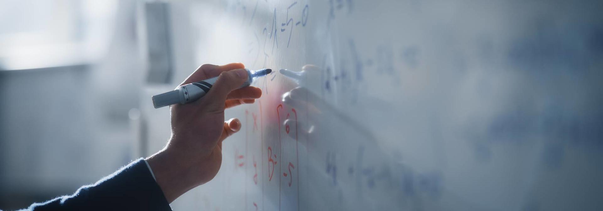 A student writing mathematical equations on a whiteboard