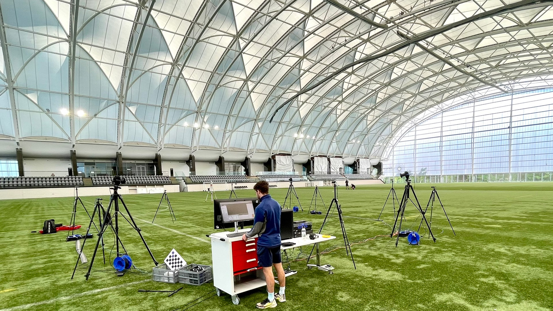 Cameras mounted on tripods as a student uses a computer on an astroturf pitch in the Oriam sports centre.