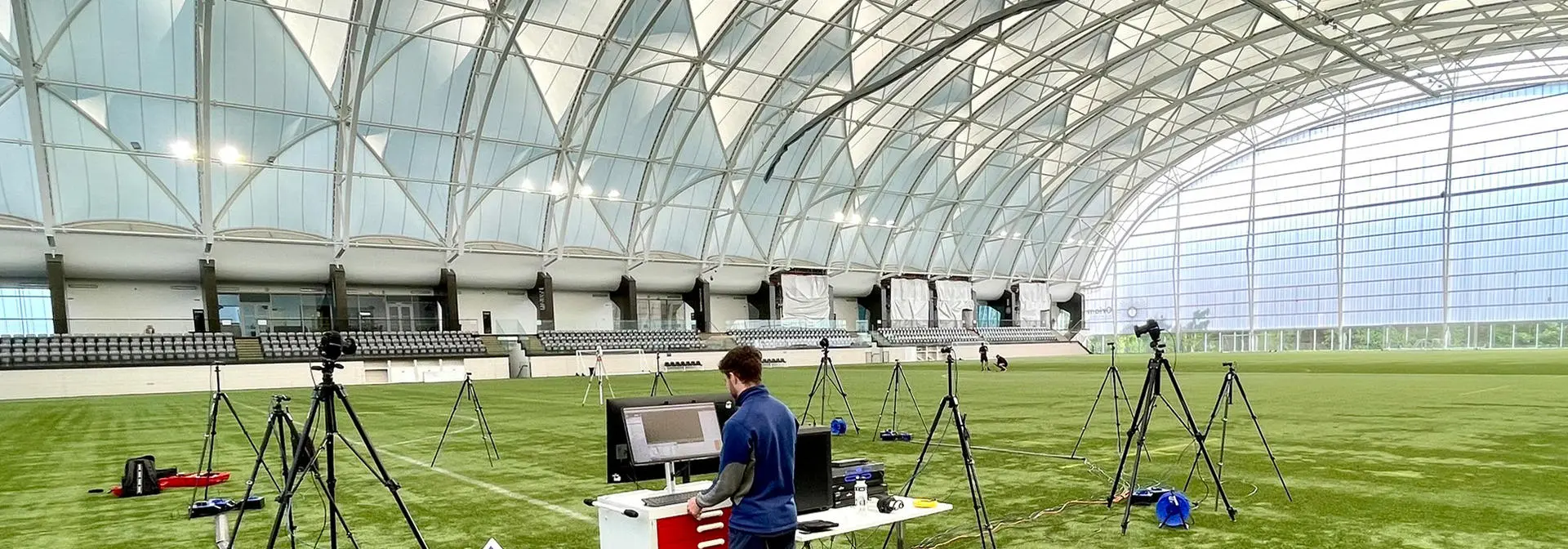 Cameras mounted on tripods as a student uses a computer on an astroturf pitch in the Oriam sports centre.