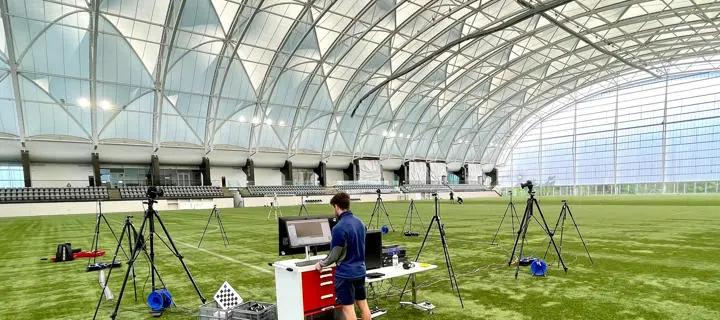 Cameras mounted on tripods as a student uses a computer on an astroturf pitch in the Oriam sports centre.
