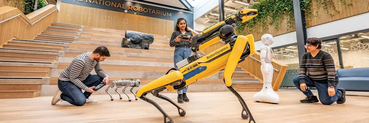 Students operate two robot dogs using handheld controllers in the National Robotarium