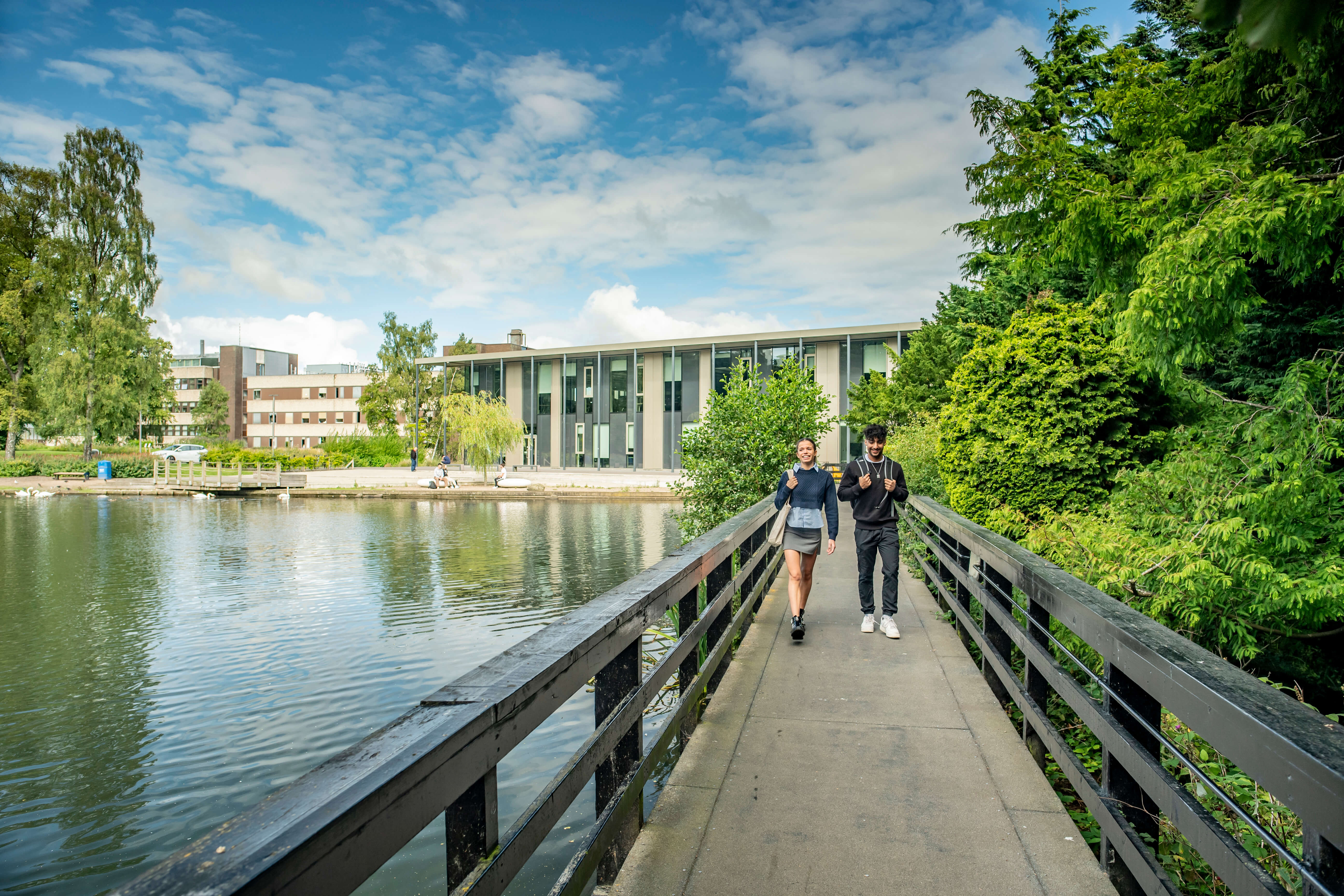 Two students walk across the bridge over the loch with GRID building in the background, Edinburgh Campus.