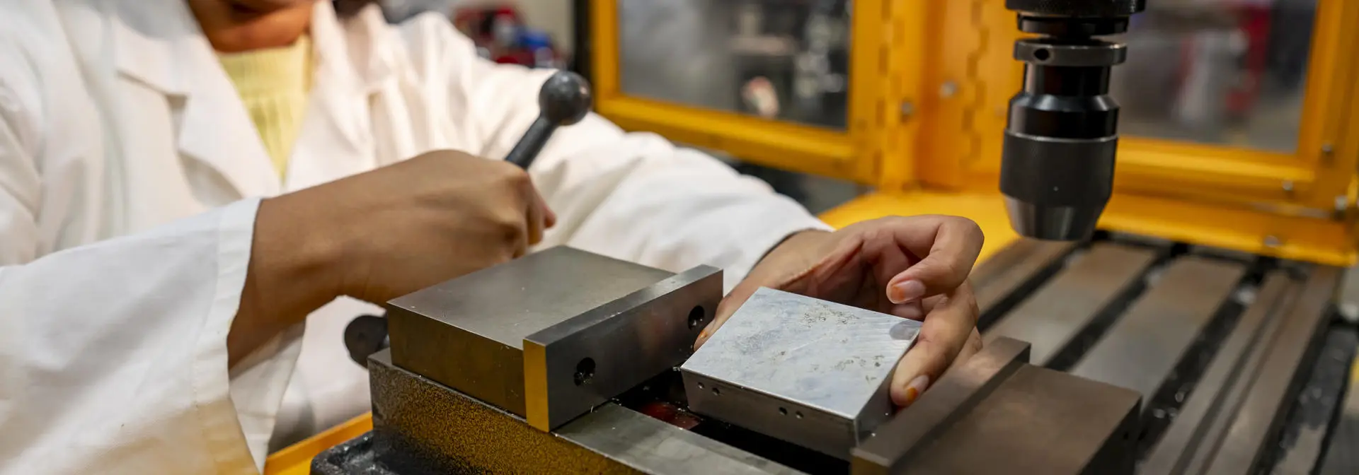 Engineering student wearing safety glasses places a piece of metal in a bench vice