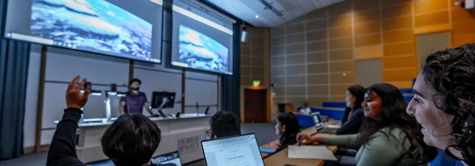 A student holds up his hand to ask a question in a lecture theatre