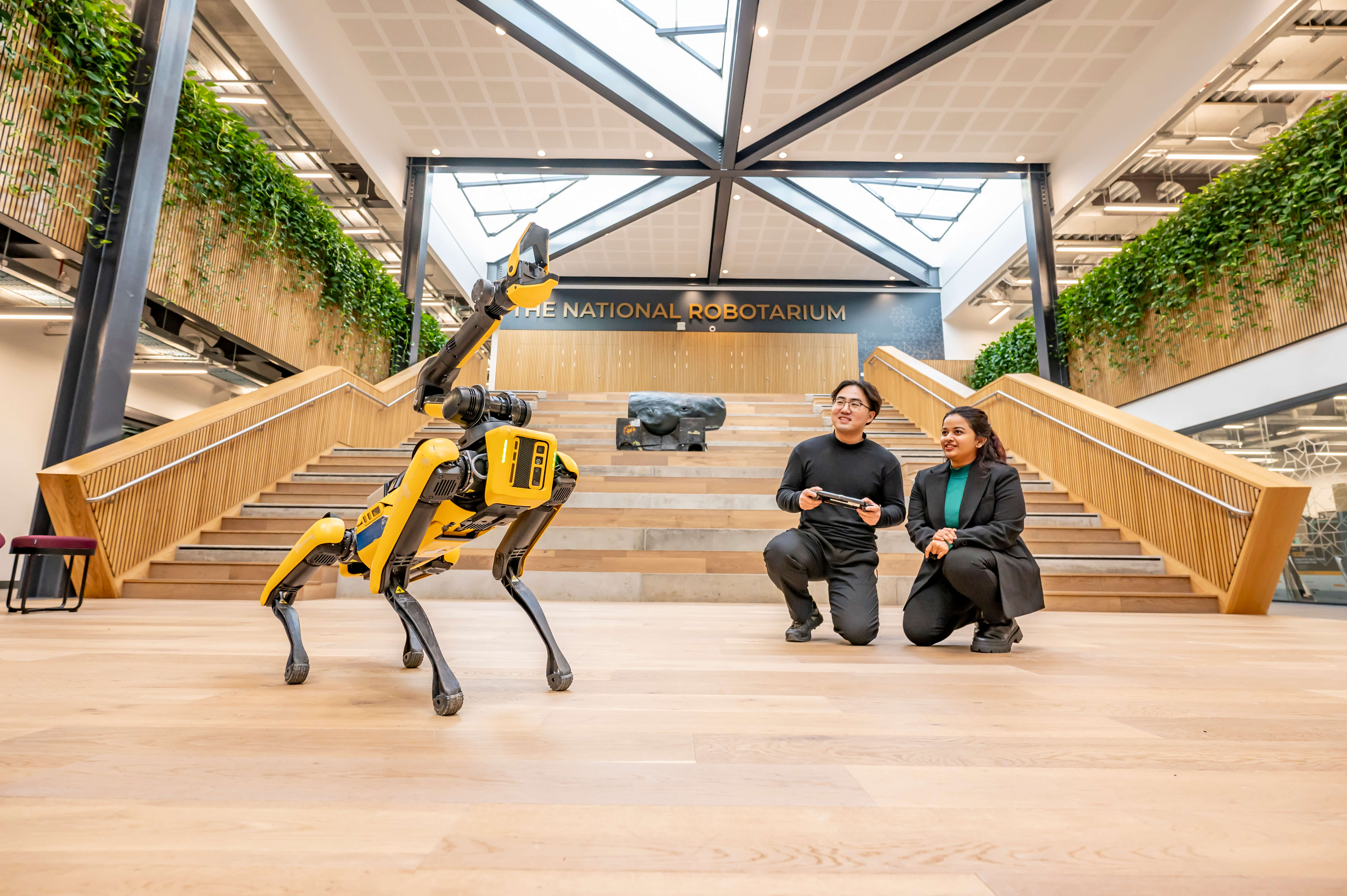 A pair of students controlling the claw attachment of a yellow four-legged robot.
