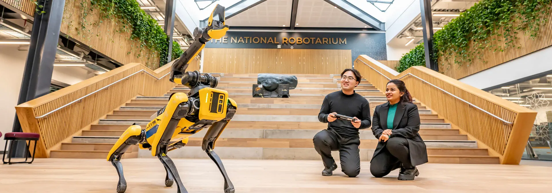 A pair of students controlling the claw attachment of a yellow four-legged robot.