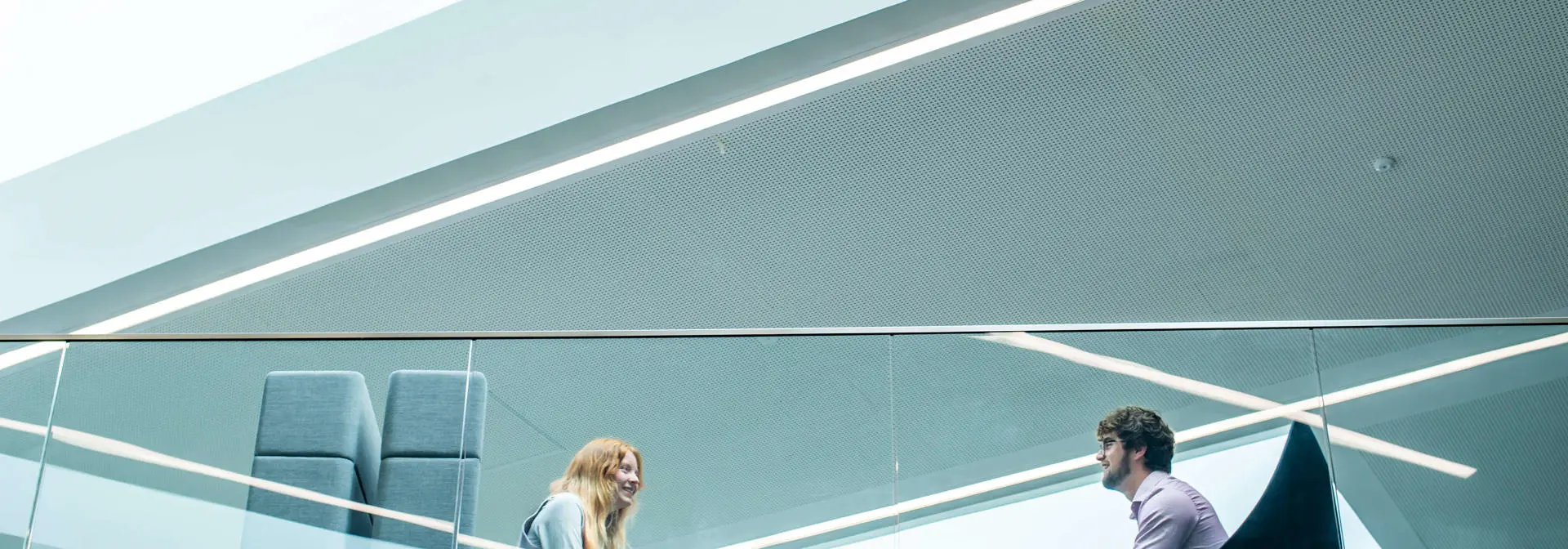 Two students seated opposite one another on the mezzanine floor of the GRID building viewed from the ground floor