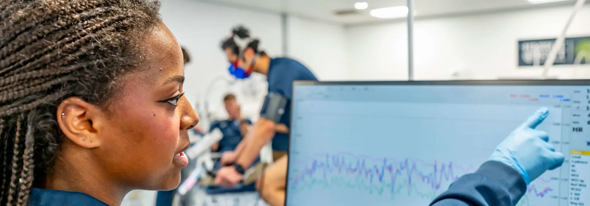 A Sport and Exercise Science student monitors a cyclist's performance data on a computer monitor