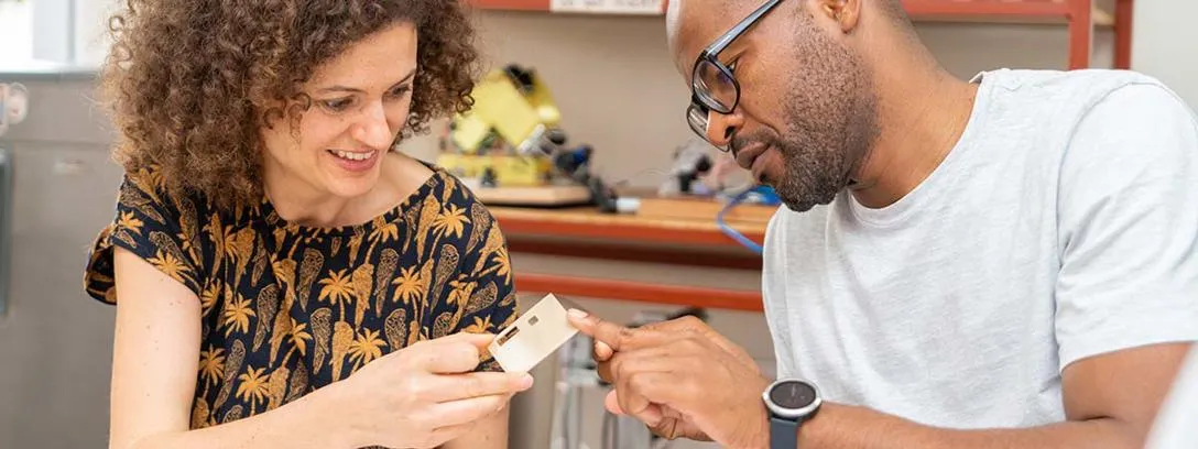 Participants of the first Frugal Diagnostics workshop in Accra, December 2023, inspect a part of a prototype device made in Ashesi University Fab Lab. Two people look at a small device