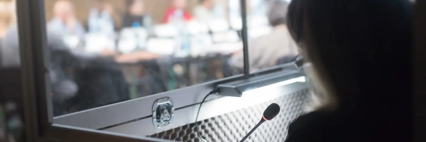 A person sits in a booth interpreting and translating an event