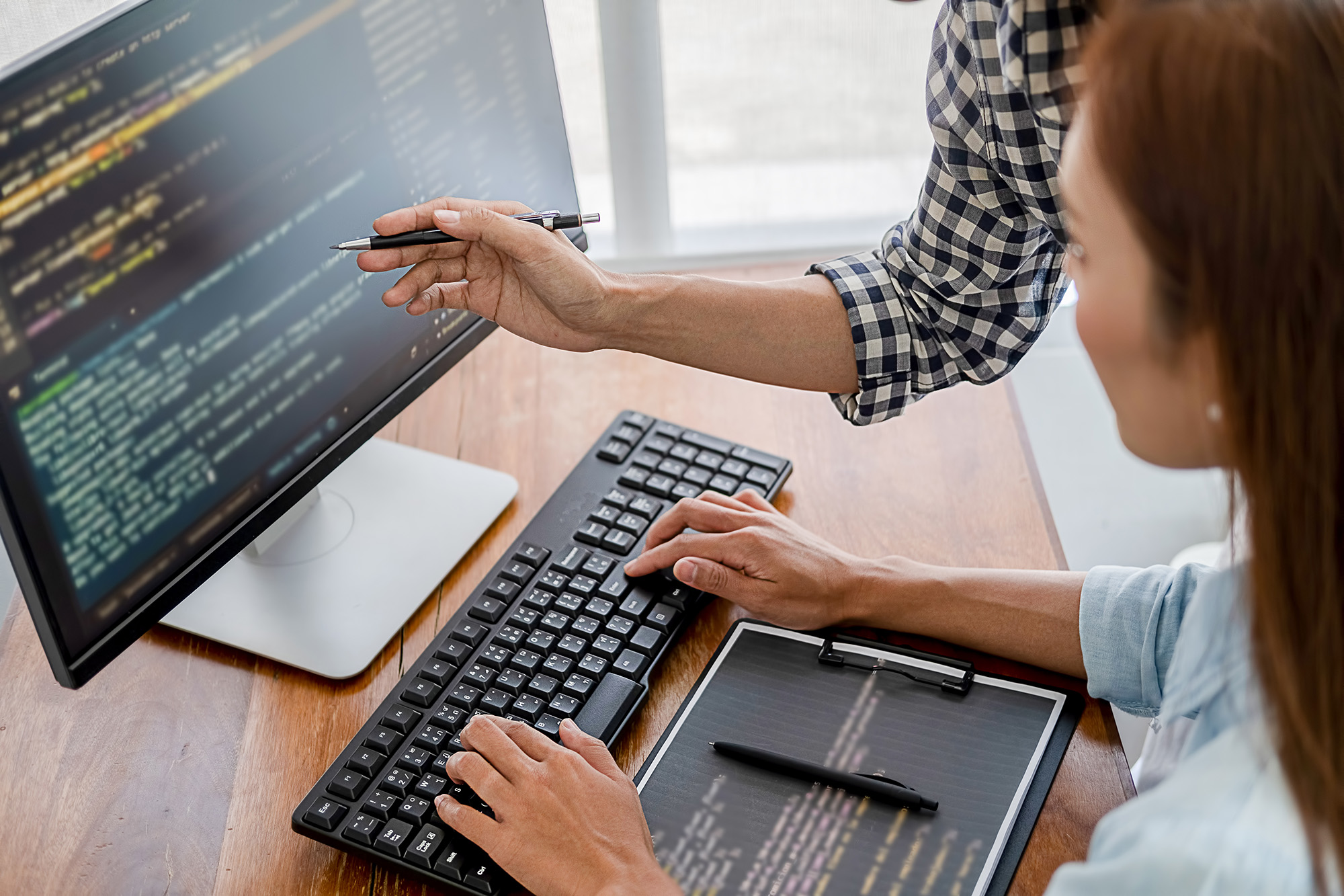 Woman coding on a desktop computer in discussion with a colleague