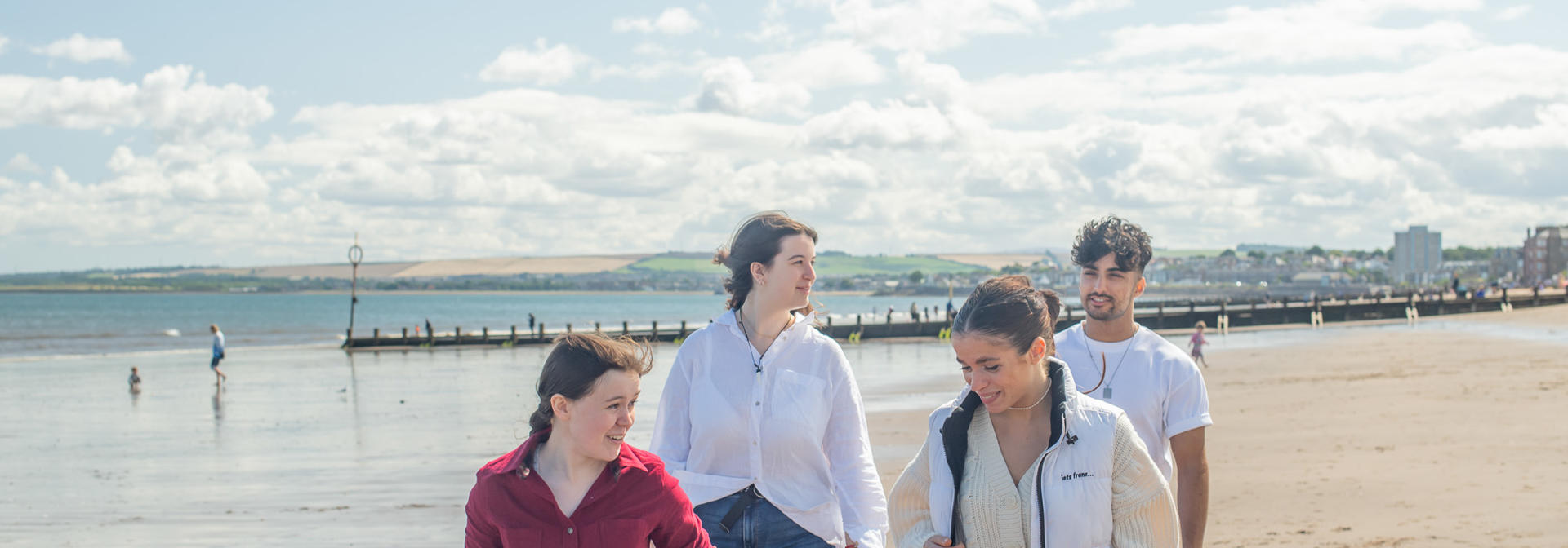 Four individuals walking on a beach on a sunny day.