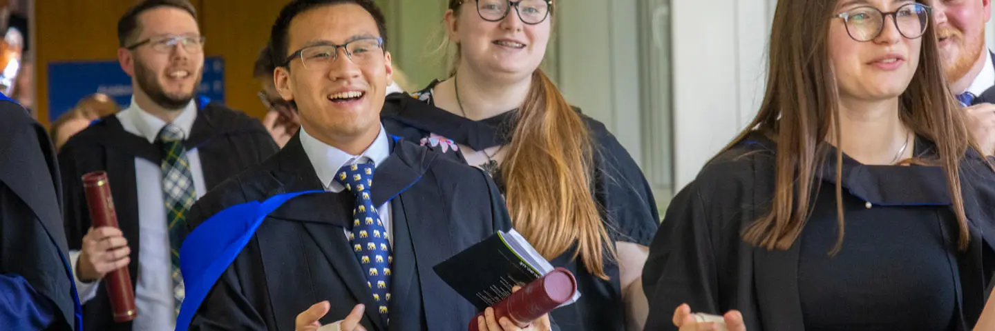 Graduates smiling and walking down the corridor of Edinburgh campus.
